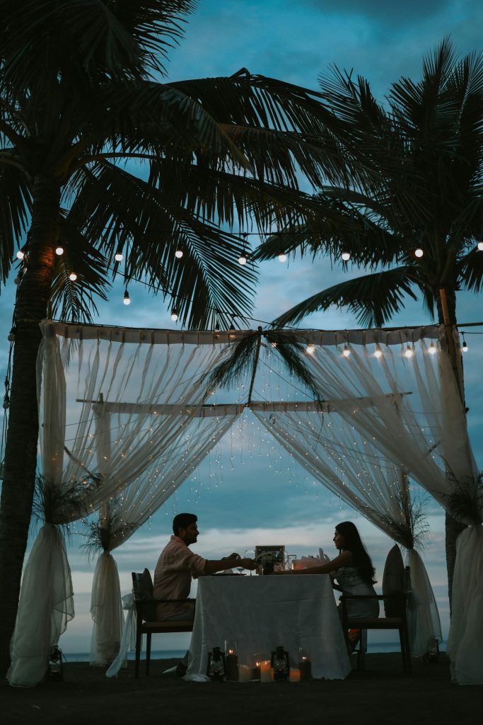 Couple having romantic dinner under palm trees at dusk.